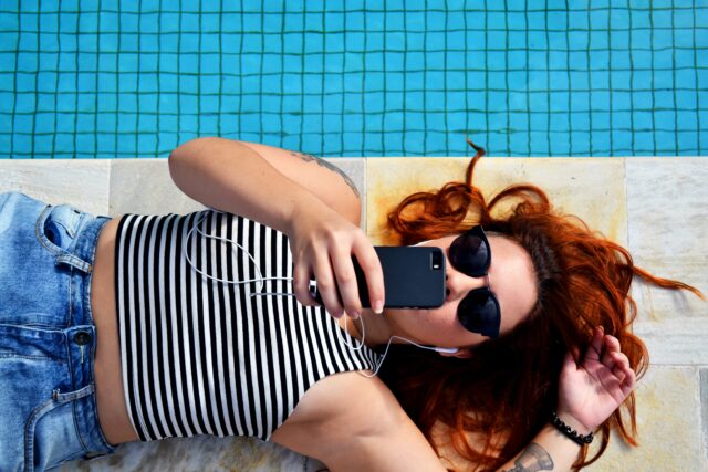 A woman in sunglasses using an in-app payment solution to make a purchase by a pool.