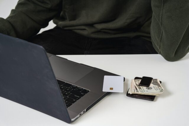 A person sit next to a table with a laptop, credit card, and cash