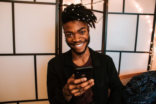 A young man smiles while holding a smartphone and using a wallet payment method.