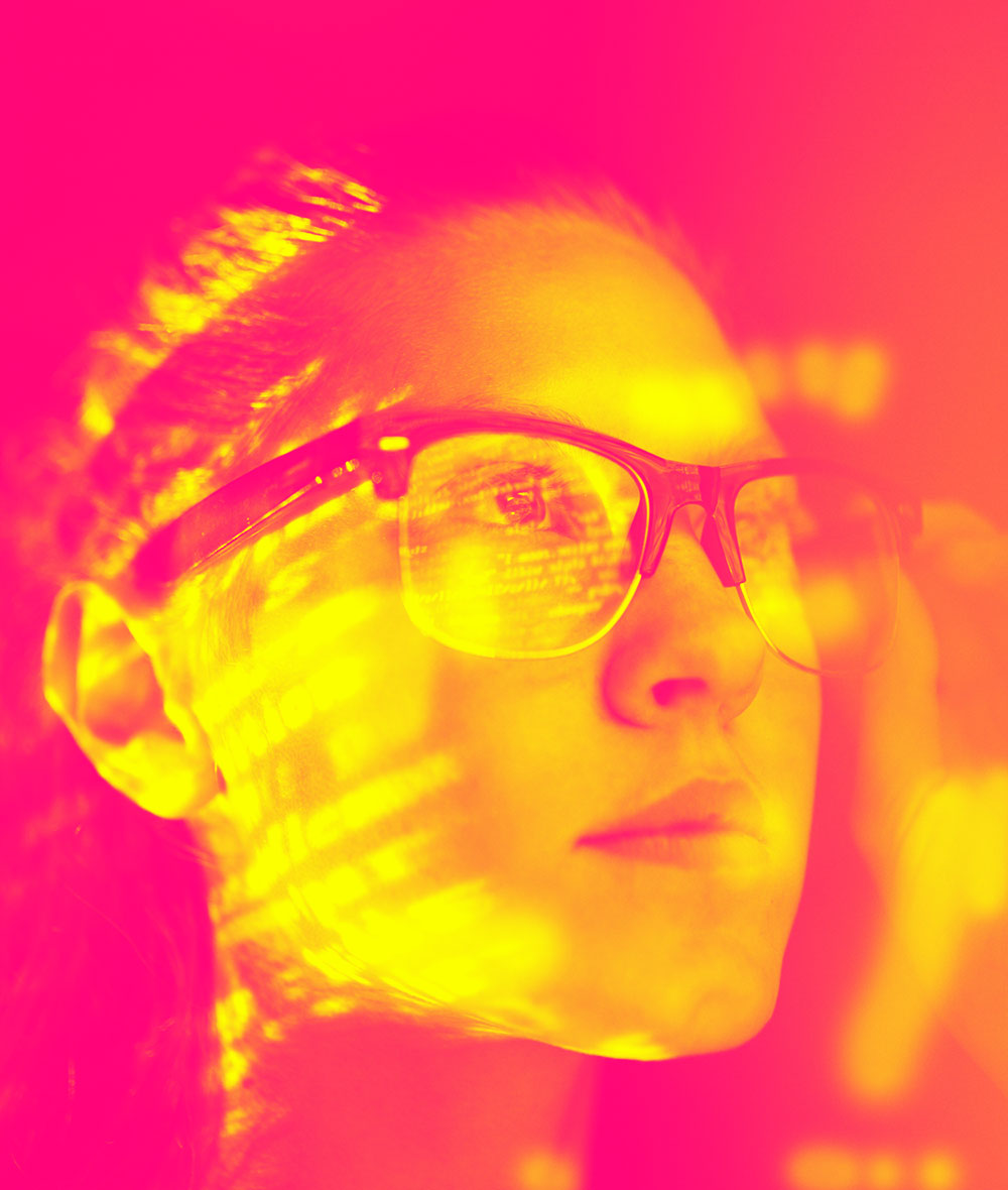 A developer's computer screen is reflected in her glasses.