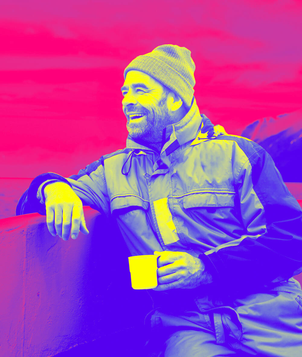 A guy in winter clothes and a glass of hot drink, leaning his hand and smiling