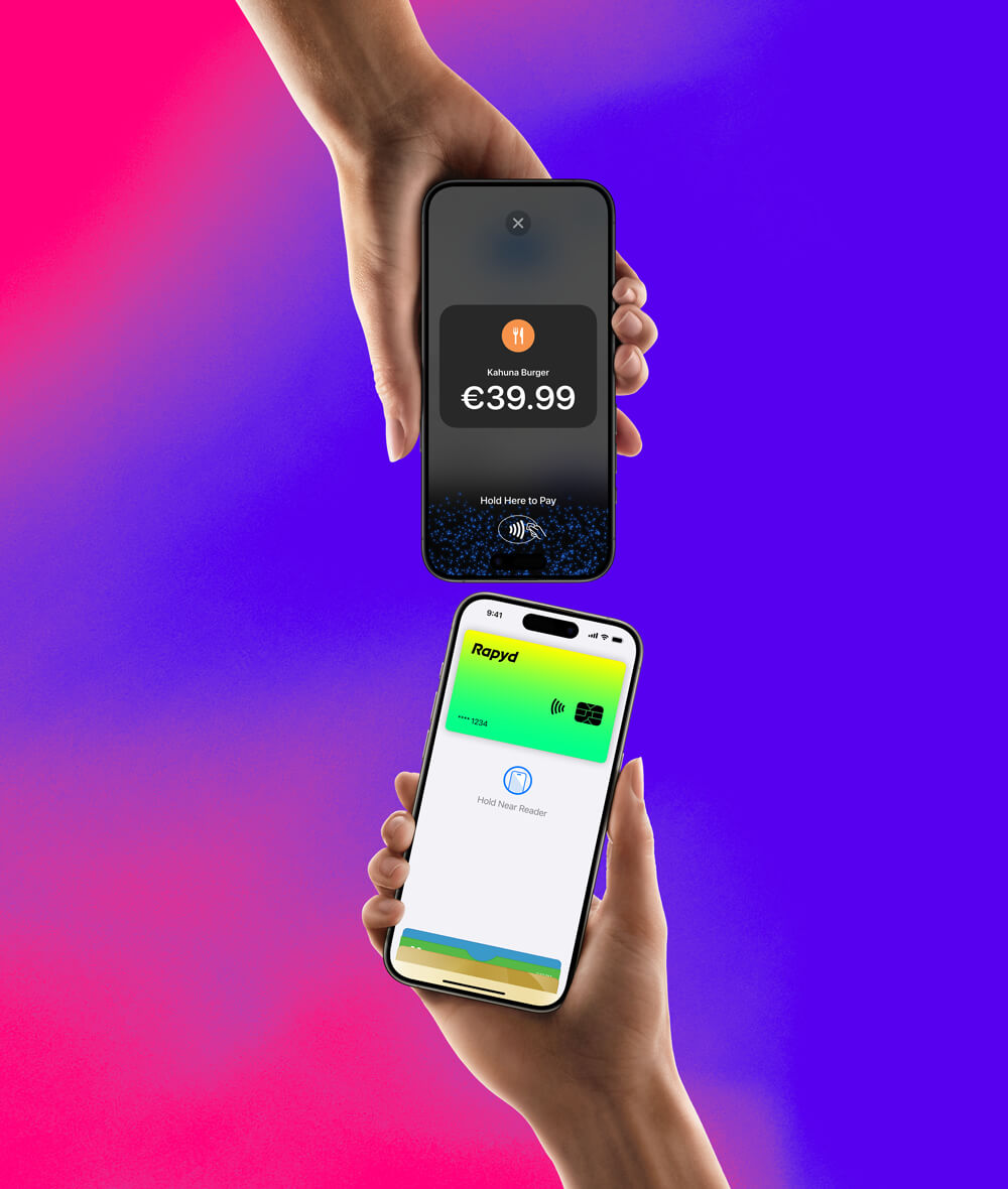 A hand holding an iPhone with a Rapyd credit card is about to pay on an iPhone that has a hold here to pay screen on it.
