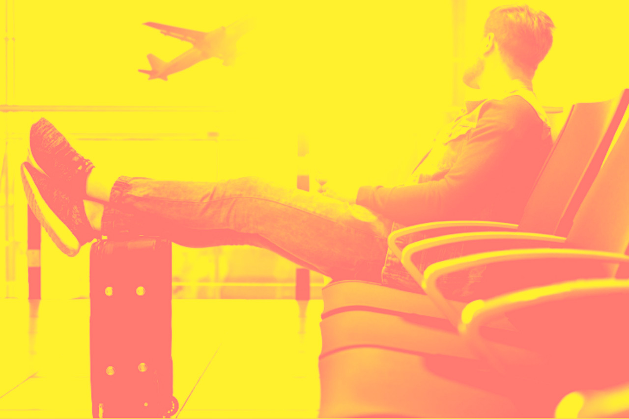 A man sits cross-legged at an airport and watches a plane take off.