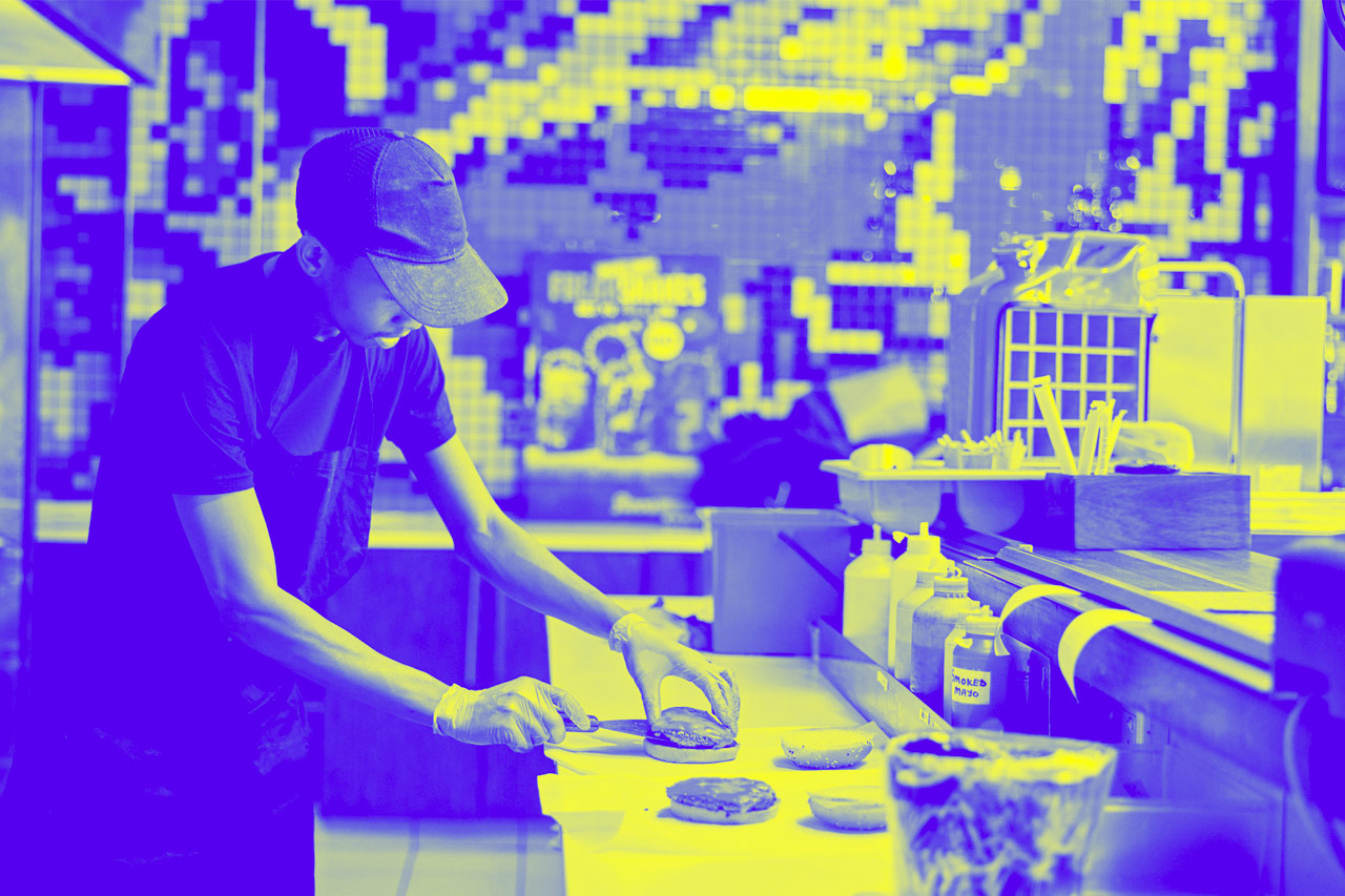 A burger and fast food kitchen worker at counter with gloves, cooking and uniform at small business.