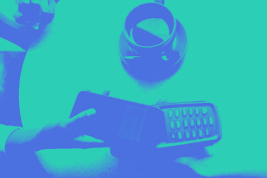 A man passes his phone over a payment terminal on a table with coffee on it.