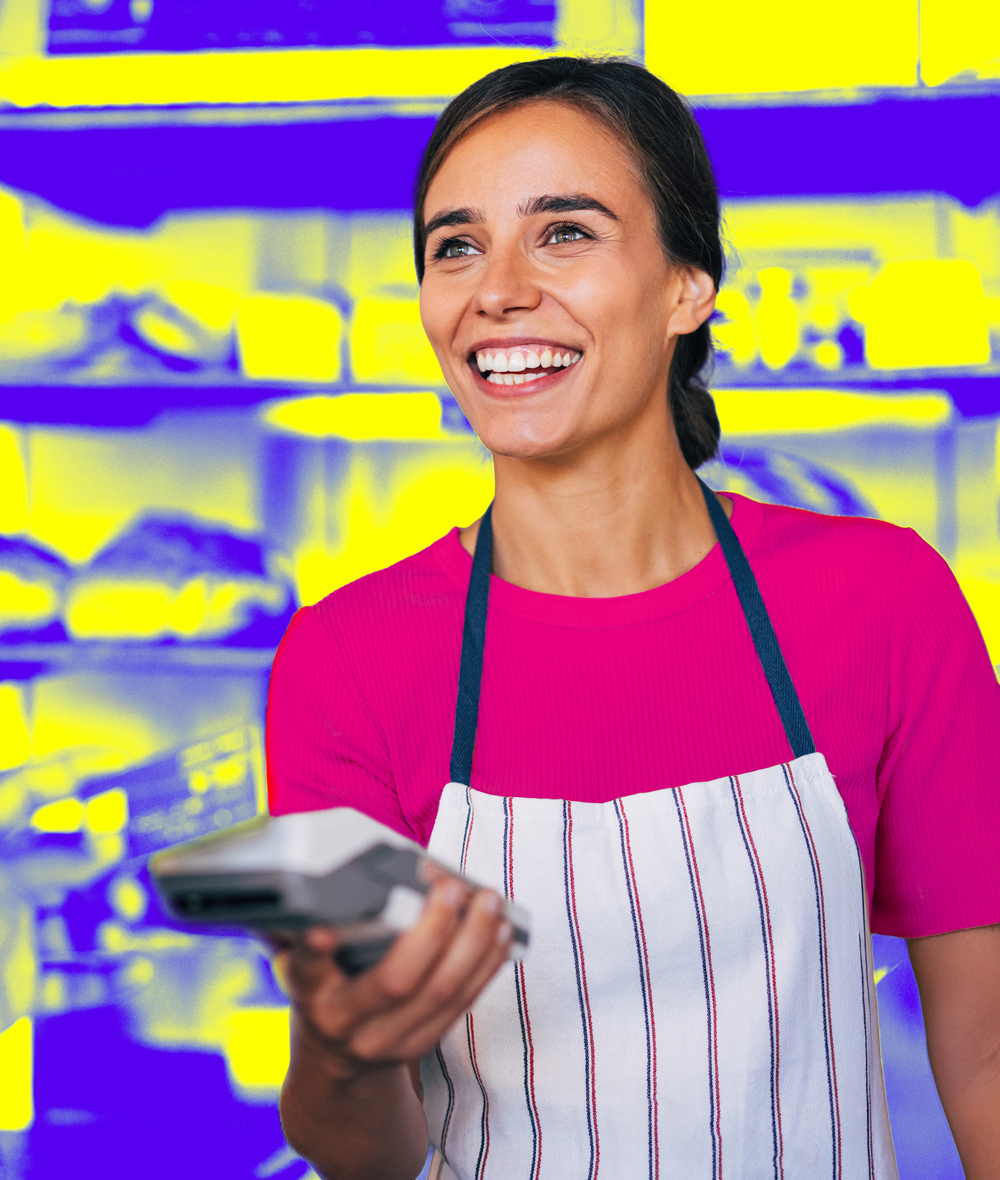A saleswoman in a store holds a payment terminal and hands it to a customer to pay.