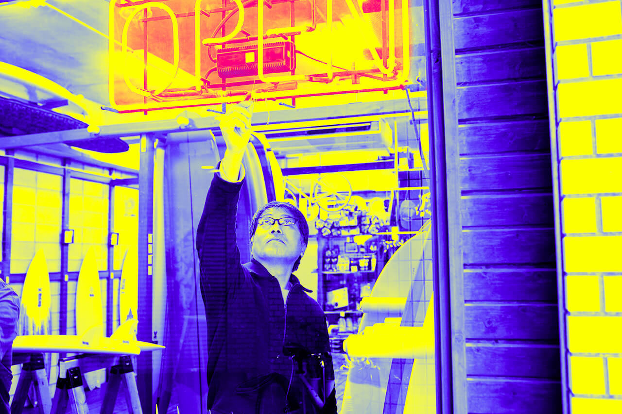 An Asian salesperson raises his hand and turns on the store's sign.