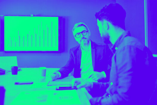 wo business professionals, one older and one younger, are sitting in a conference room having a serious discussion.