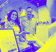 Happy Latin American couple shopping and making a mobile payment with their cell phone at a clothing store