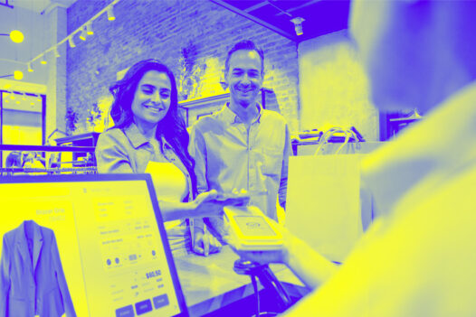 Happy Latin American couple shopping and making a mobile payment with their cell phone at a clothing store